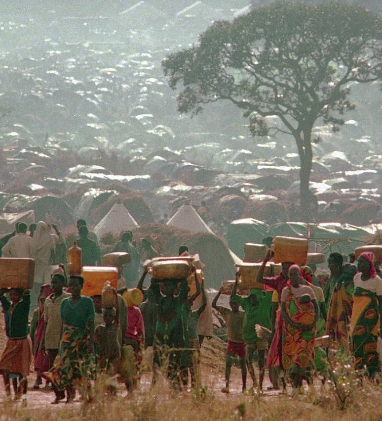 Refugees who fled the ethnic bloodbath in neighboring Rwanda carry water containers back to their huts at the Benaco refugee camp in Tanzania, May 17, 1994. (AP Photo/Karsten Thielker)